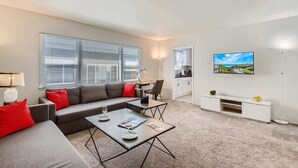 Una sala de estar moderna con un sofá gris, cojines rojos, una mesa de centro y un televisor en la pared.