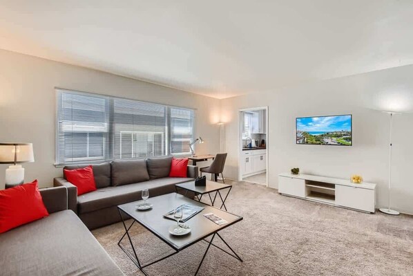 A modern living room with a grey sofa, red cushions, a coffee table, and a TV on the wall.