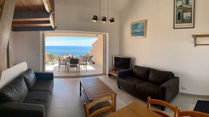 A living room with a sofa, a wooden table, and a TV. There's a balcony with a table and chairs, and a painting on the wall. - Casa di Toro, facing the sea, rated 4 *, swimming pools, Palombaggia beaches 1.9KM. (Porto-Vecchio)