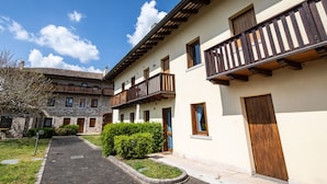 Un cortile con un vialetto lastricato, un edificio in pietra con balconi in legno e un edificio moderno con porte in legno.