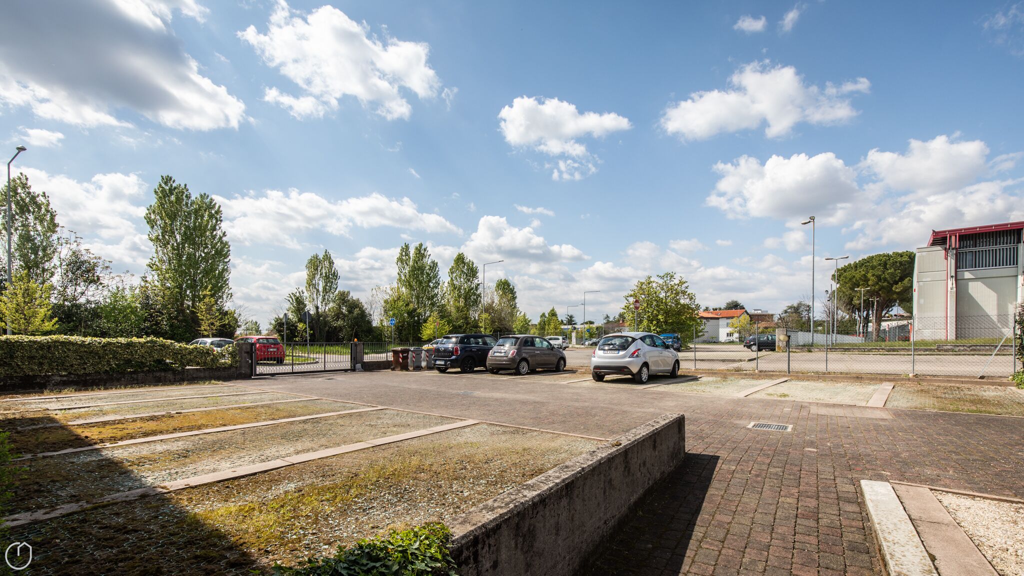 A parking area with cars, a fence, and a building in the background.