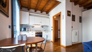 Una cucina moderna con mobili bianchi, un forno a microonde e un piano cottura. Nell'area soggiorno, si trova un tavolo da pranzo con sedie e un divano blu.