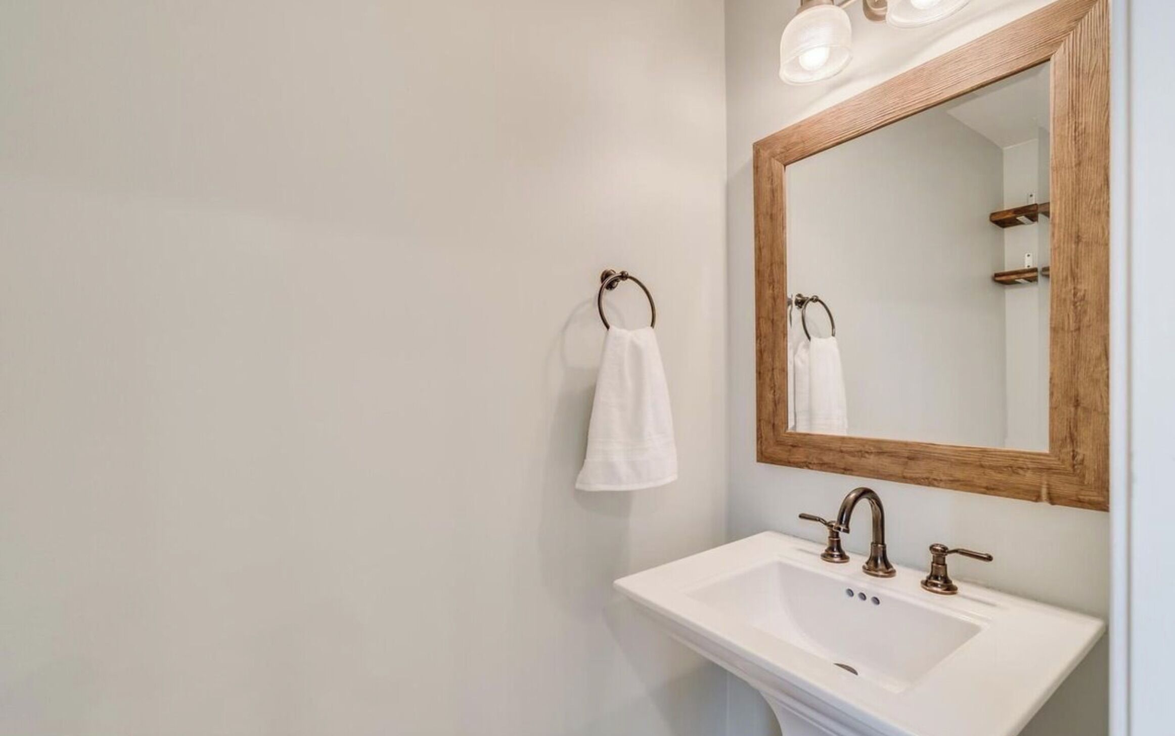 A bathroom with a white sink, a wooden-framed mirror, and a towel hanging on a ring.