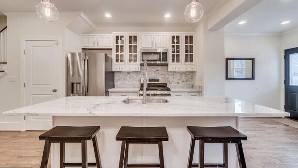 Una cocina moderna con armarios blancos, una isla grande con taburetes de bar, electrodomésticos de acero inoxidable e iluminación colgante.