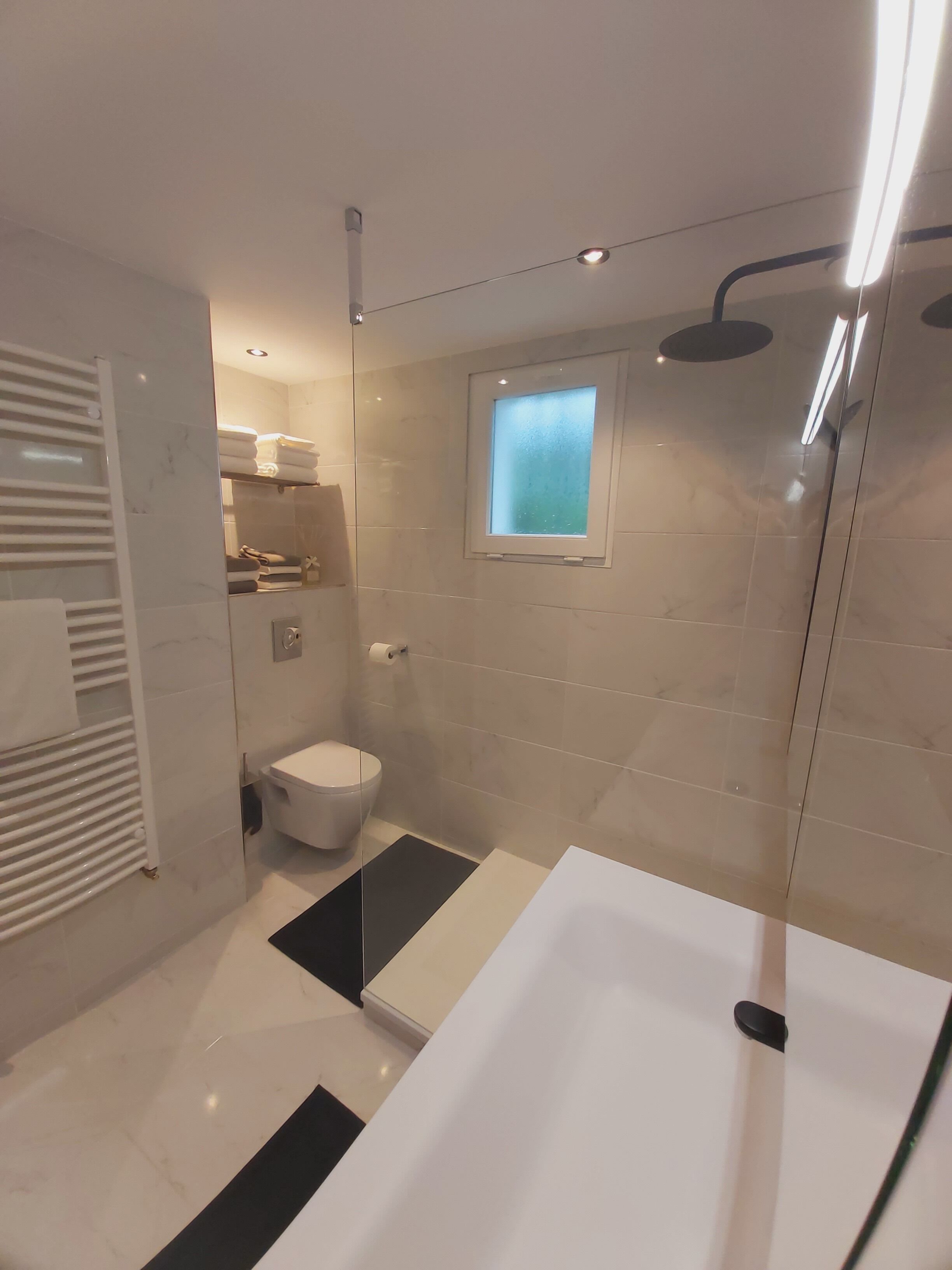 A modern bathroom with a glass-enclosed shower, a white bathtub, and a toilet.