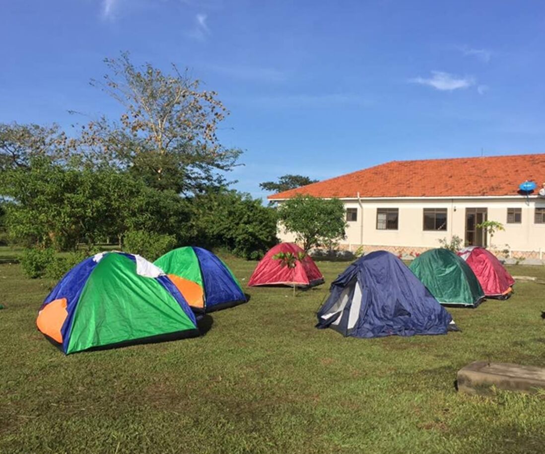 A grassy area with several colorful tents and a building with a red roof in the background.