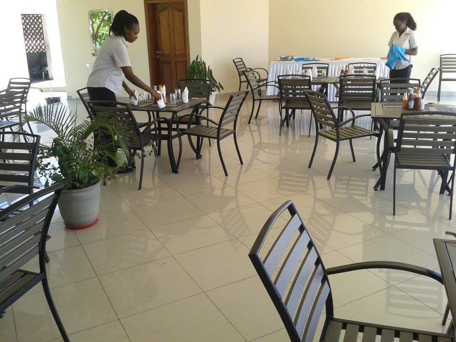 Comedor con mesas, sillas, una planta en maceta y una persona limpiando.