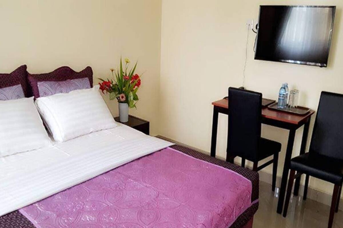 Habitación de hotel con cama, escritorio, dos sillas, televisor y un florero con flores.
