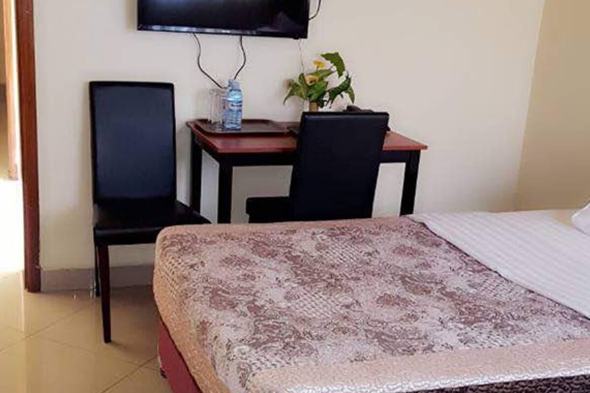 Habitación de hotel con cama, escritorio con silla, televisión montada en la pared y planta en maceta.