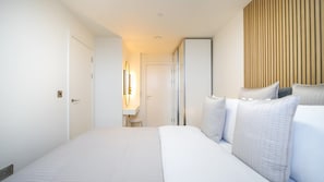 A hotel room with a bed, a bedside table, a mirror, and a wall-mounted light fixture.