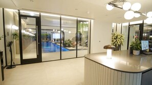 A reception area with a counter, a seating area with chairs, and a view of a pool through glass doors.