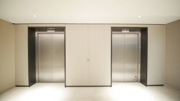 A hallway with three elevator doors, a light-colored floor, and a plain wall.