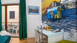 Habitación de hotel con cama, escritorio, silla, mesita pequeña y balcón con vistas.