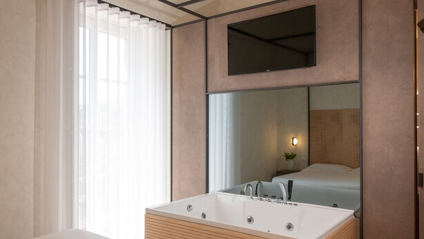 Une salle de bain moderne avec une grande baignoire, un miroir et une fenêtre ornée de rideaux légers.