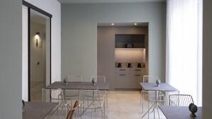 Un espace repas moderne avec une table et des chaises, un coin cuisine doté de placards et d’appareils électroménagers, et une vue à travers une porte vitrée.