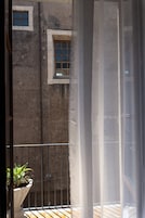A balcony with a potted plant, a window, and a metal railing.