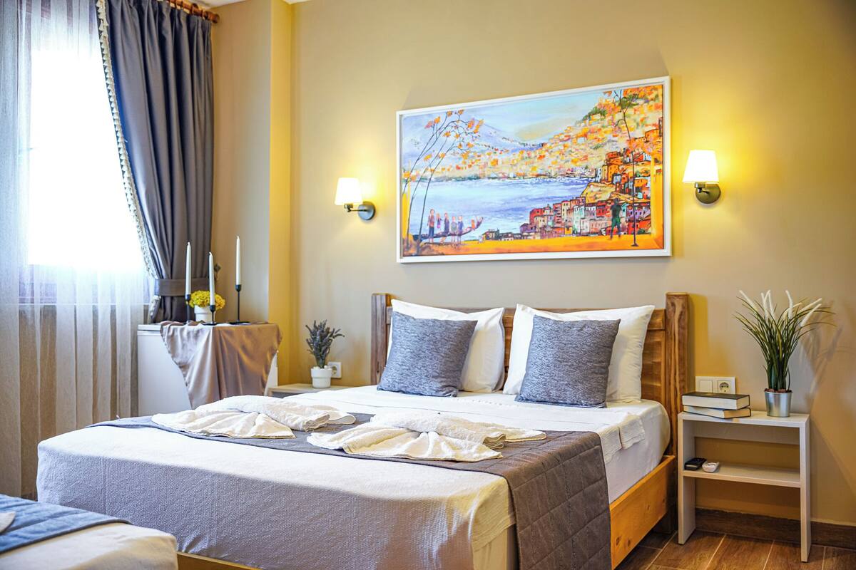 A hotel room with a bed, bedside tables, a painting, and a window with curtains.