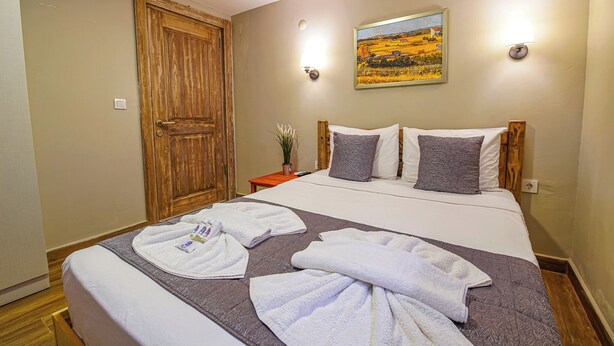 Habitación de hotel con puerta de madera, cama con ropa de cama blanca y gris, y dos luces fijadas a la pared.