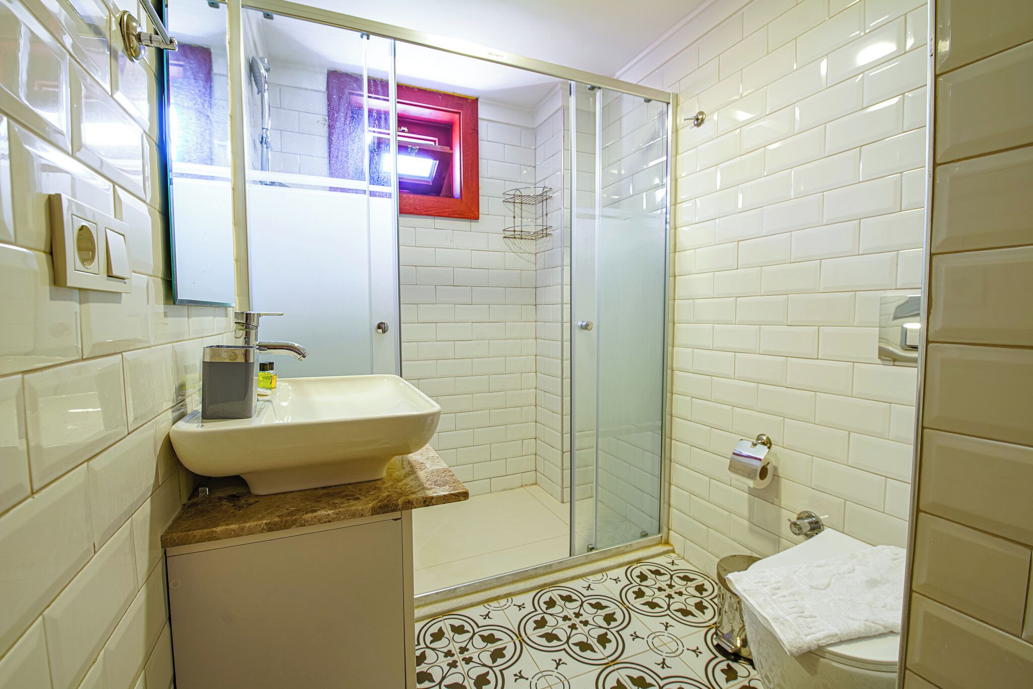 A bathroom with a white sink, a glass shower enclosure, and patterned floor tiles.