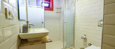 A bathroom with a white sink, a glass shower enclosure, and patterned floor tiles.