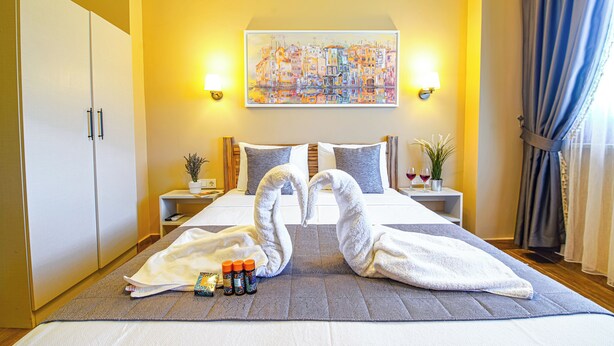 A hotel room with a bed, two nightstands, a painting on the wall, and a window with curtains. - Bakbay Bozcaada (Bozcaada)