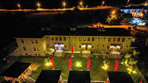 A large building with multiple windows and a central entrance. There are outdoor seating areas with tables and chairs, and red umbrellas. - Bakbay Bozcaada (Bozcaada)