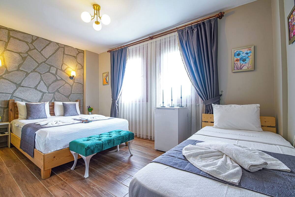 A hotel room with two beds, a stone wall, a wooden floor, and a window with curtains.