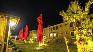 A courtyard with outdoor seating and umbrellas, surrounded by a building with multiple windows and a staircase. - Bakbay Bozcaada (Bozcaada)