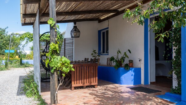 A covered patio area with a wooden bench, potted plants, and a blue and white wall. - Casa Nora T2 (Castro Marim)