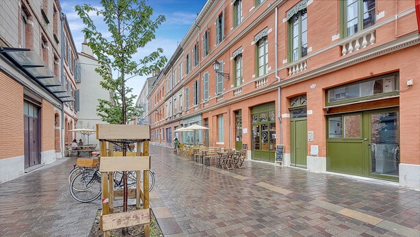 Une rue bordée de bâtiments, avec des terrasses et des vélos.