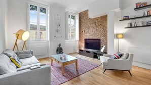 Ein modernes Wohnzimmer mit Ziegelwand, Flachbildfernseher, Sofa, Couchtisch und Bücherregal.