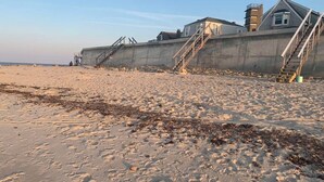 Een strand met een betonnen constructie, trappen die naar een gebouw leiden, en een heldere lucht.