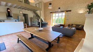 Ein geräumiger Wohnbereich mit einem Holztisch, einer Bank und einem blauen Sofa. Eine Treppe führt zu einer oberen Ebene.