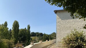 Ein Gebäude aus Stein mit geneigtem Dach, umgeben von einer niedrigen Steinmauer und Topfpflanzen.