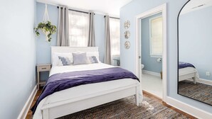 A bedroom with a bed, bedside table, hanging plant, window with curtains, and a mirror. - Hot Tub Oasis • Parking • 1 Block to King St! (Charleston)