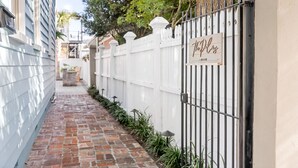 A narrow brick pathway flanked by a white fence and a building with a sign that reads "The Plugs." - Hot Tub Oasis • Parking • 1 Block to King St! (Charleston)