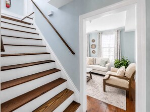 A staircase with wooden steps and a handrail, leading to a living room with a sofa, a coffee table, and a plant.