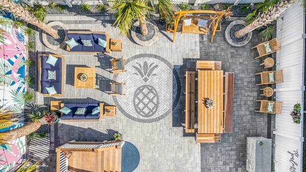 Un espace patio extérieur doté d’un aménagement circulaire pour s’asseoir, d’une table en bois et d’un élément décoratif central en mosaïque.