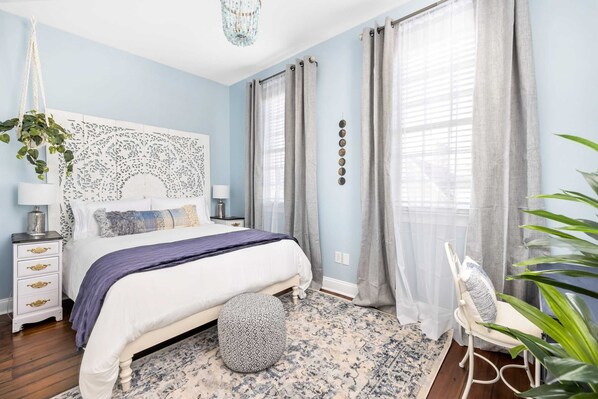A bedroom with a bed, bedside table, lamp, and a hanging plant. - Hot Tub Hideaway • Parking • 1 Block to King St! (Charleston)