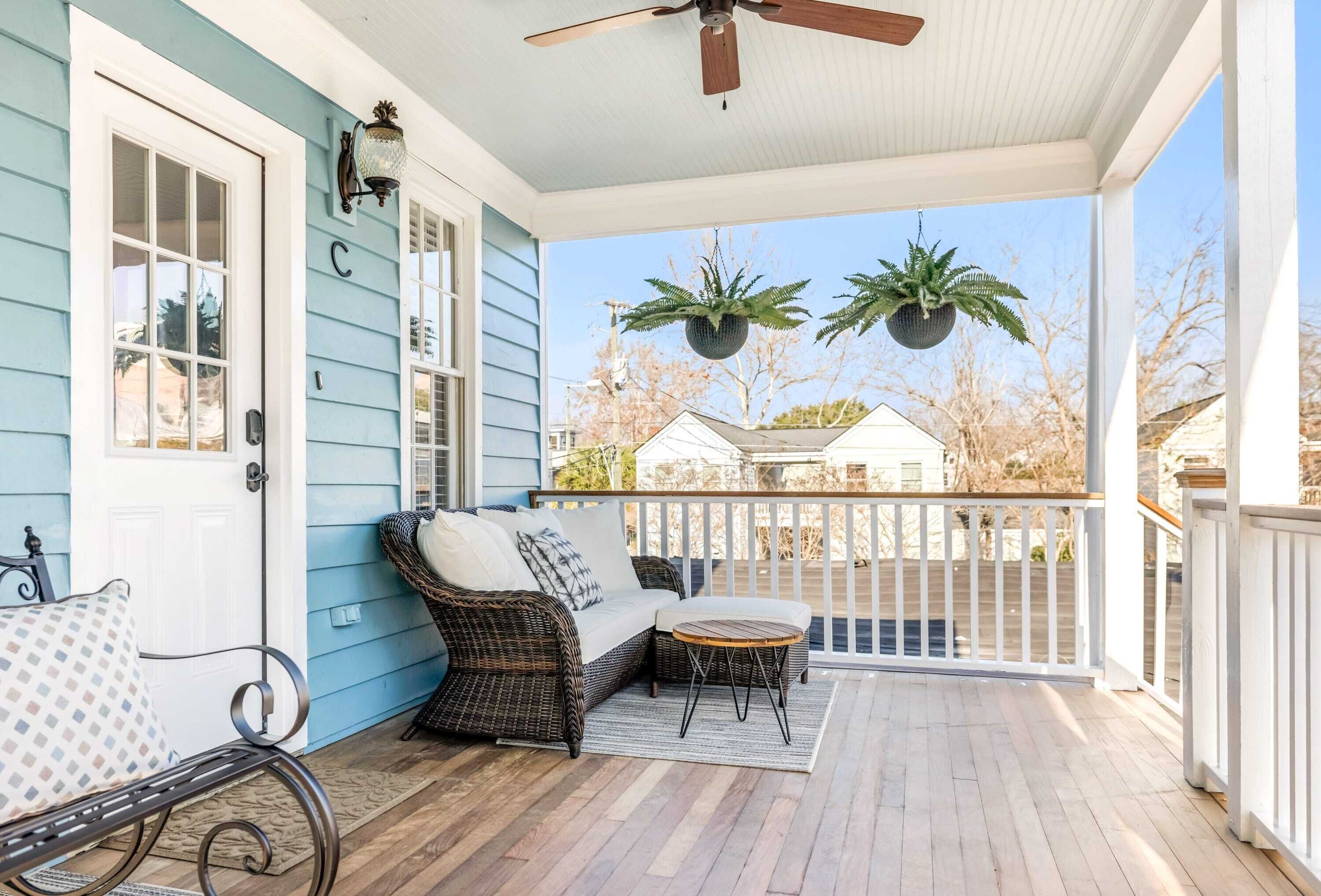 A porch with wicker furniture, a ceiling fan, and hanging planters.