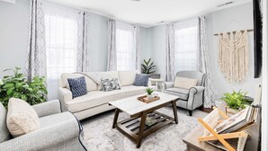 Un salon comprenant un canapé, des fauteuils, une table basse et une décoration murale en macramé.