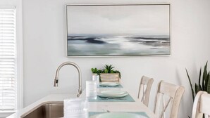 A modern kitchen with a white countertop, stainless steel sink, and a dining area with a table set for two. - Hot Tub Getaway • Parking • 1 Block to King St! (Charleston)