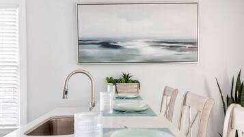 A modern kitchen with a white countertop, stainless steel sink, and a dining area with a table set for two.