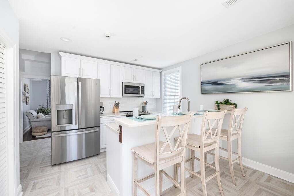 A modern kitchen with white cabinets, stainless steel appliances, and a central island with bar stools.
