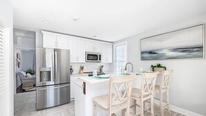 A modern kitchen with white cabinets, stainless steel appliances, and a central island with bar stools. - Hot Tub Getaway • Parking • 1 Block to King St! (Charleston)