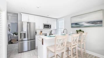 A modern kitchen with white cabinets, stainless steel appliances, and a central island with bar stools.