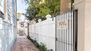 A narrow brick pathway flanked by a white fence and a building with a sign reading "The Pink Door." - Hot Tub Getaway • Parking • 1 Block to King St! (Charleston)