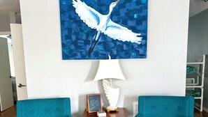 Ein Zimmer mit zwei smaragdgrünen Sesseln, einem Holztisch mit Lampe, einem gerahmten Bild und einer Wandkunst mit einem weißen Vogel.