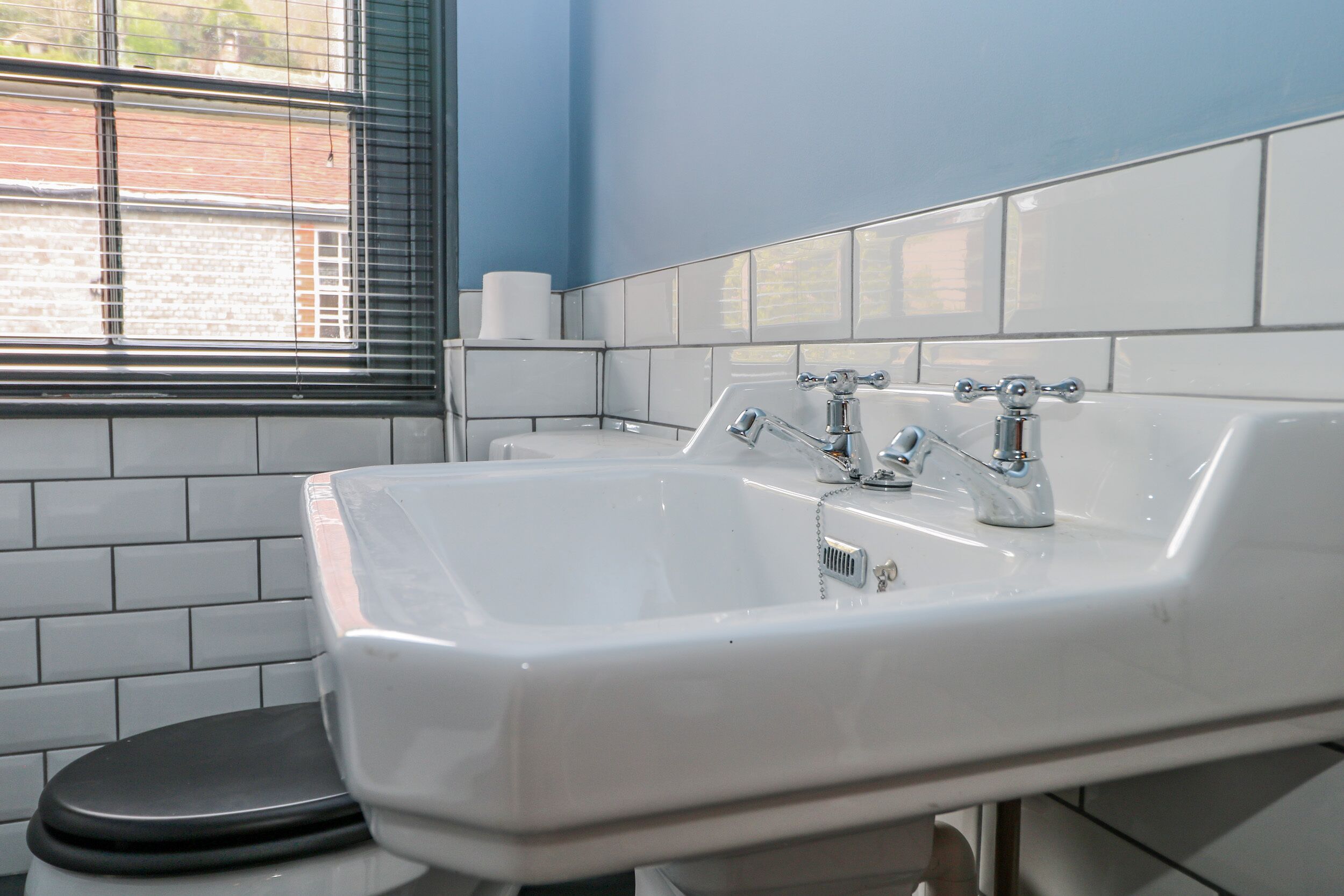 Un baño con un lavamanos blanco, un inodoro negro y una ventana con persianas.