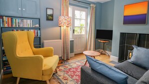 Una sala de estar con un sillón amarillo, un sofá gris, una estantería, una chimenea y una ventana con cortinas.
